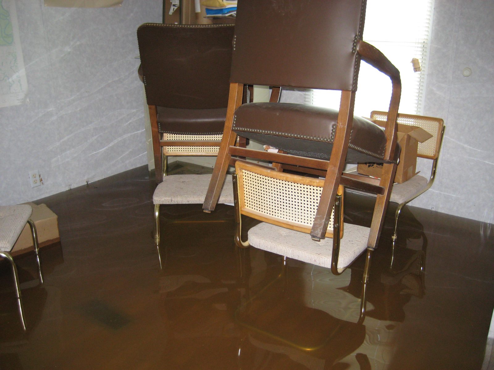 Office with brown flood water across the floor and the chairs stacked on top of each other above it