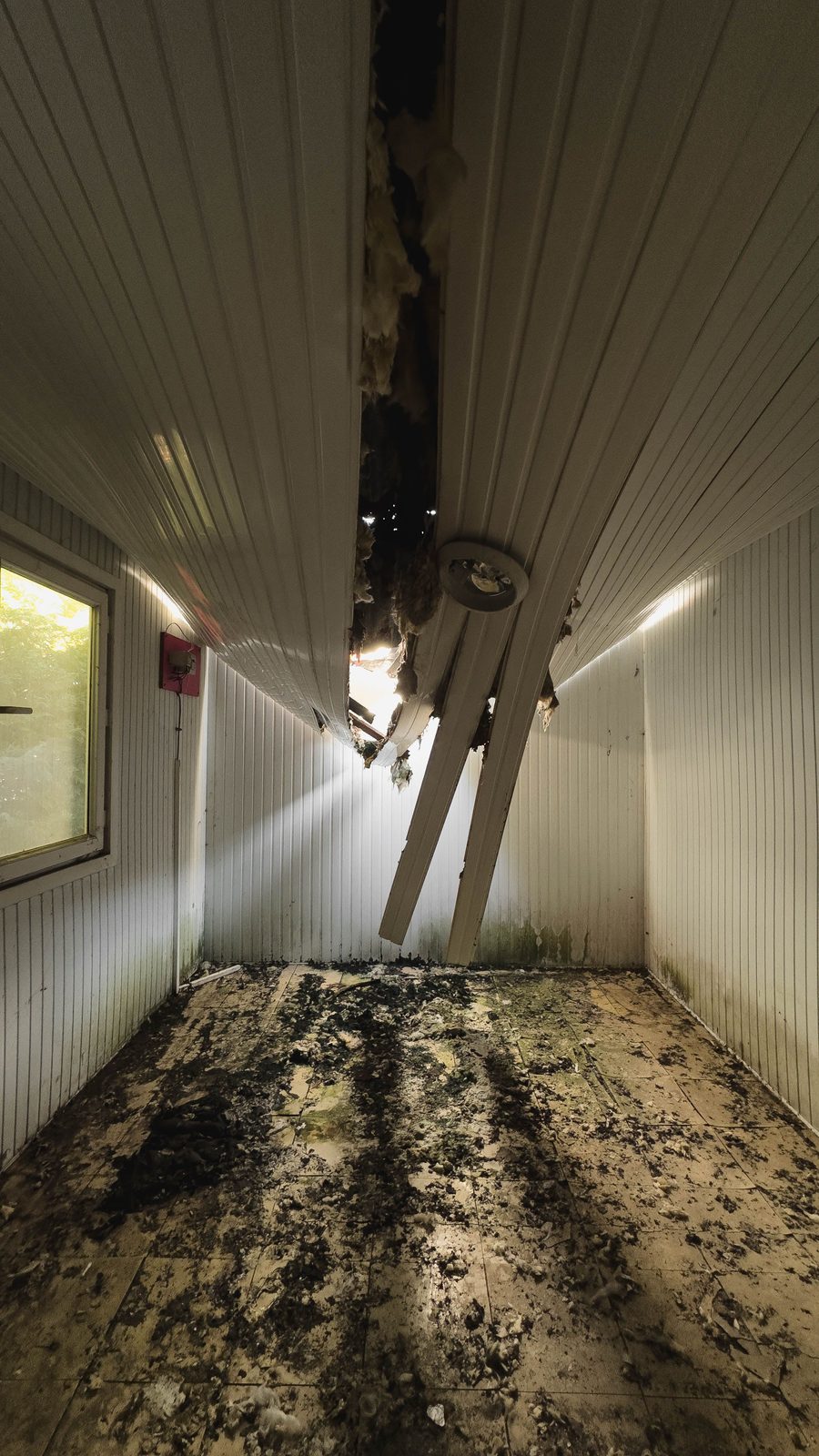Small room with the ceiling panels hanging down and debris across the tile floor after water came through from above