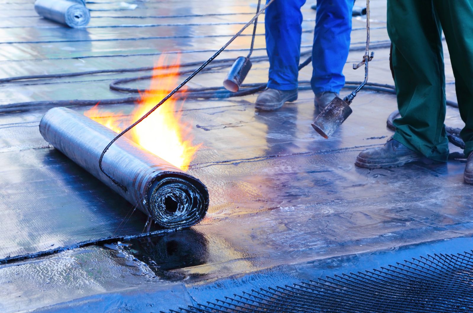 Crew torching a roll of modified bitumen membrane on a flat commercial roof