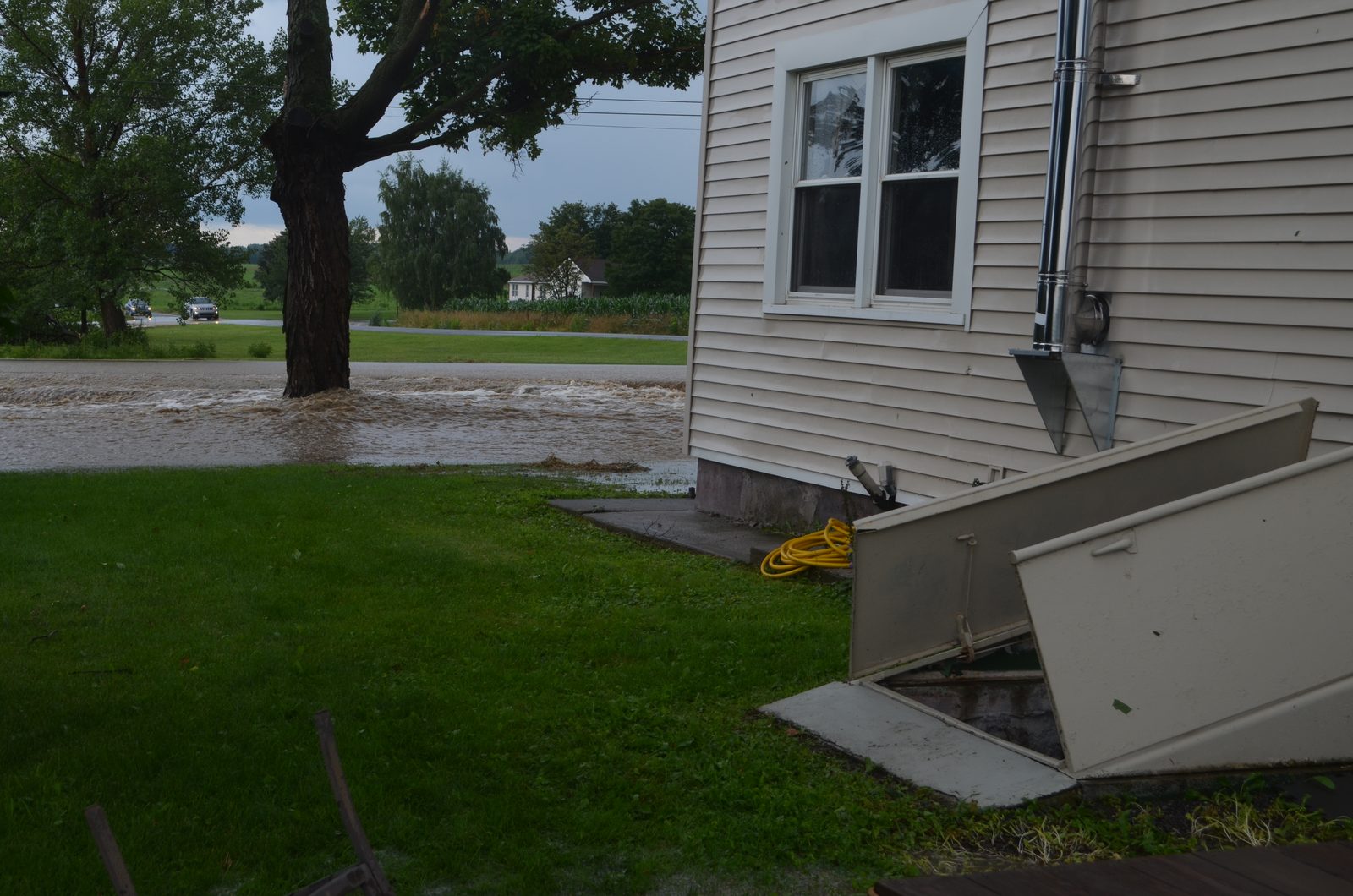 Storm water across a street and running into the open cellar door of a house