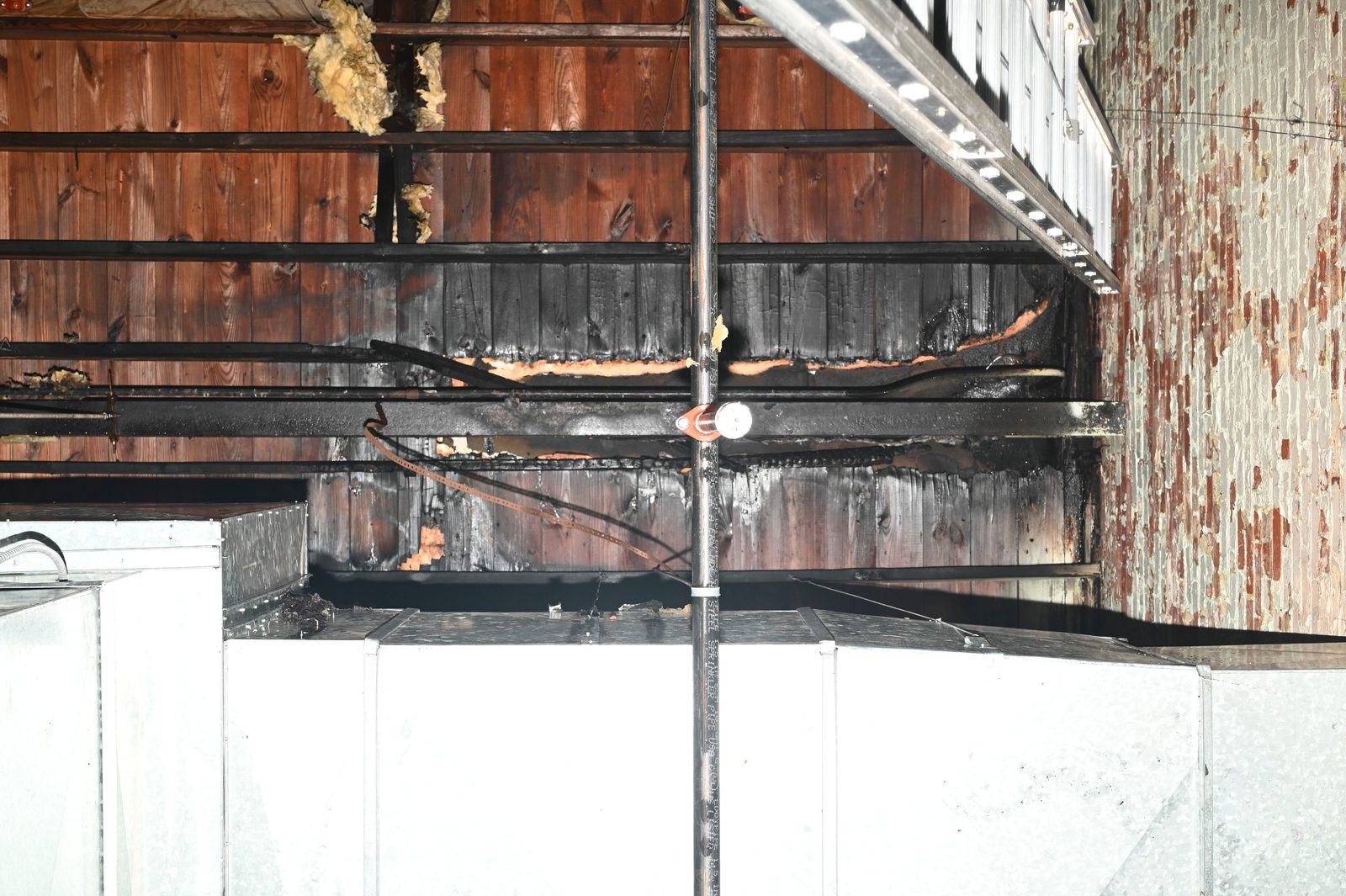 Charred wood joists above sheet-metal ductwork in a commercial building after a fire