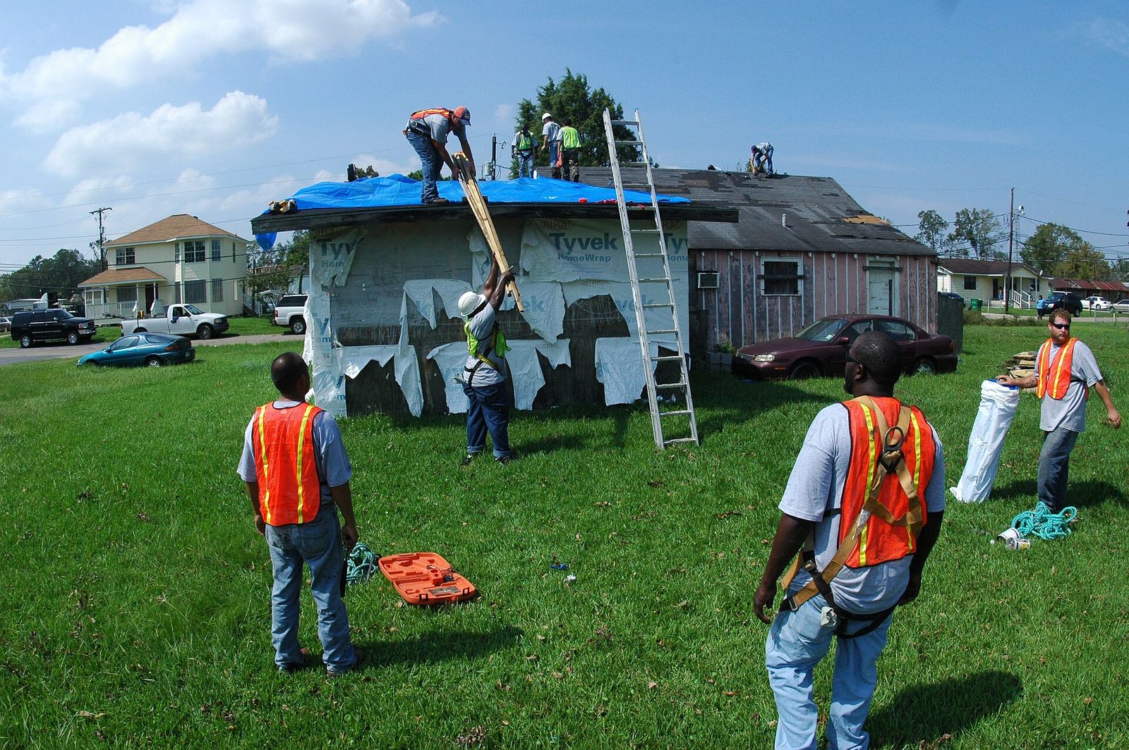 Crew in high-visibility vests tarping a storm-damaged roof from a ladder