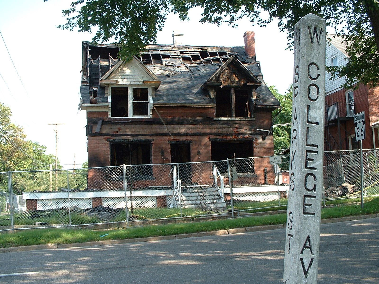 Brick two-story house with a burned-out roof and dormers behind a construction fence